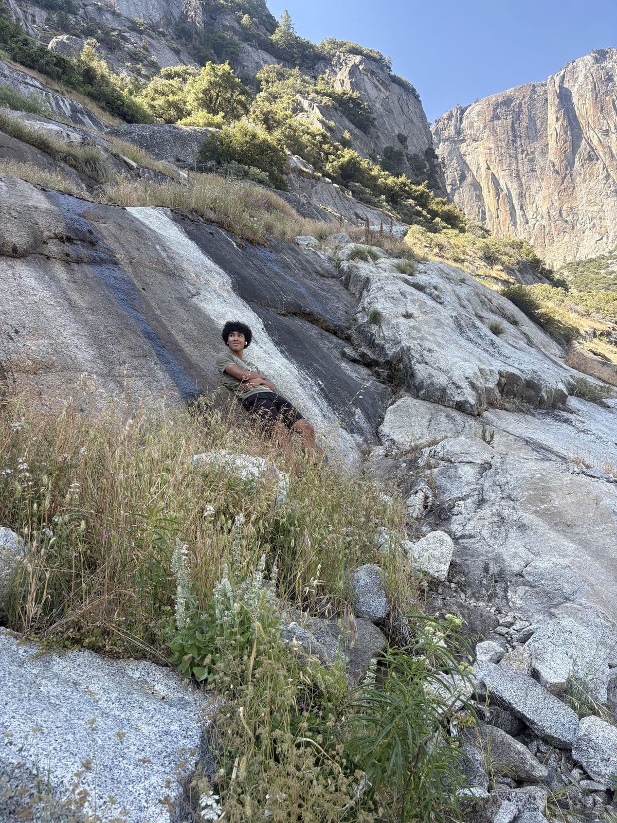 Austin Amissah resting on a granite slope in Yosemite, with cliffs behind
